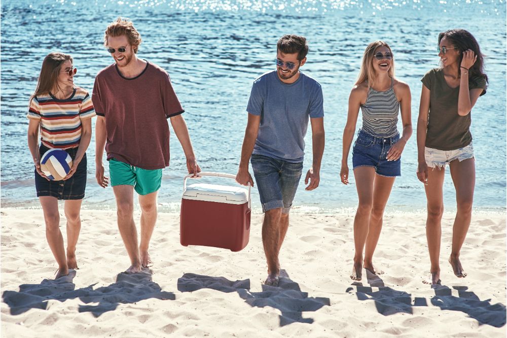 young people walking by the beach to the sea while two men carrying plastic cooler